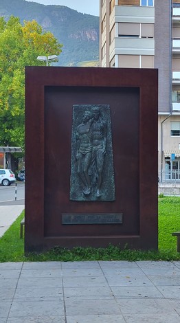 Monumento ai Caduti per la Libertà, scultura commemorativa su sfondo bronzeo in un contesto urbano.
