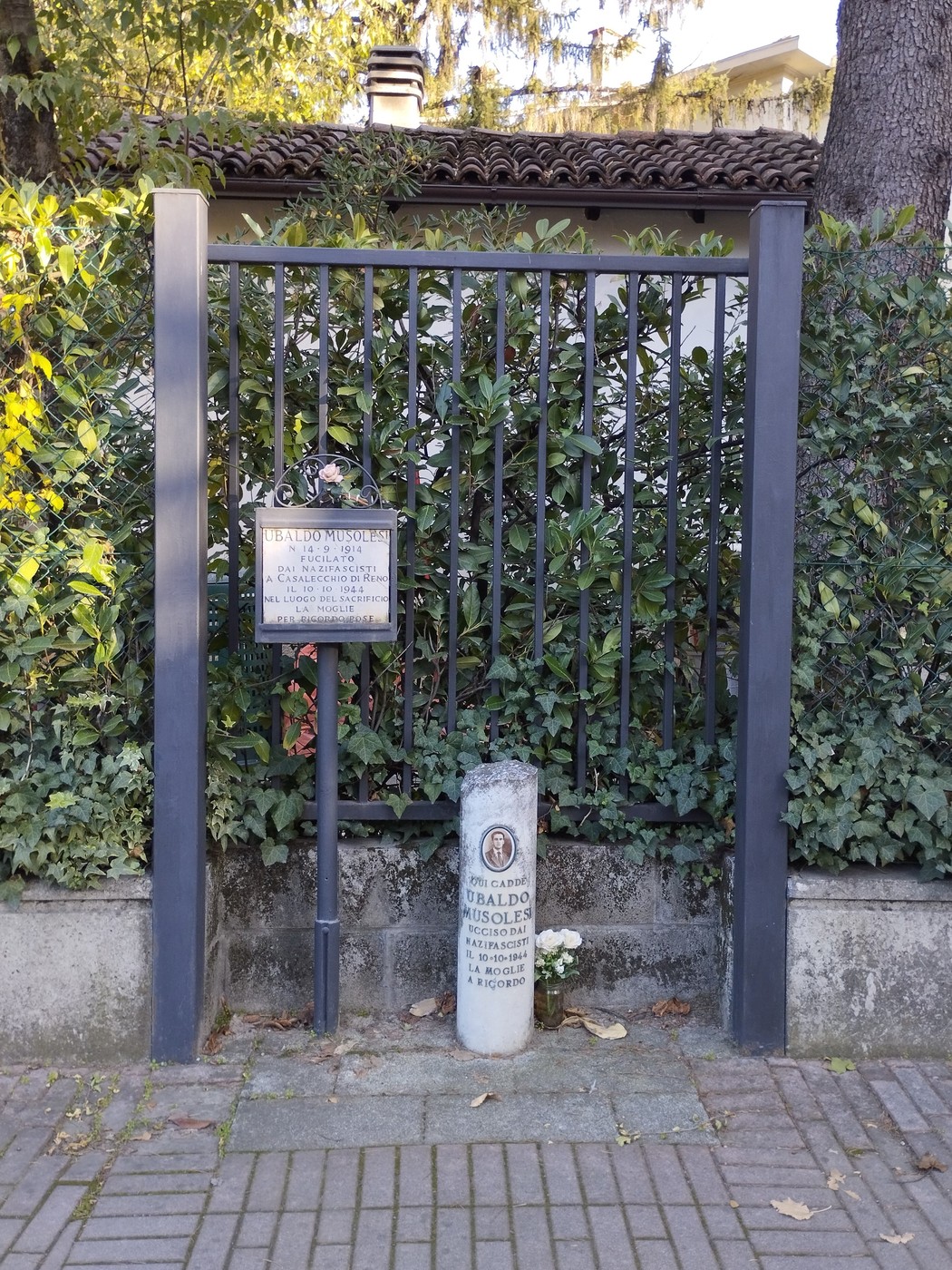 Cippo e targa commemorativa dedicati a Musolesi, situati in un contesto verde e tranquillo.