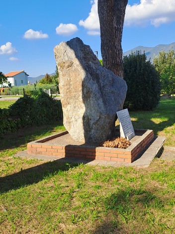 Monumento a Barachini, Barsotti e Selmi, composto da una grande pietra su base di mattoni in un ambiente verde.