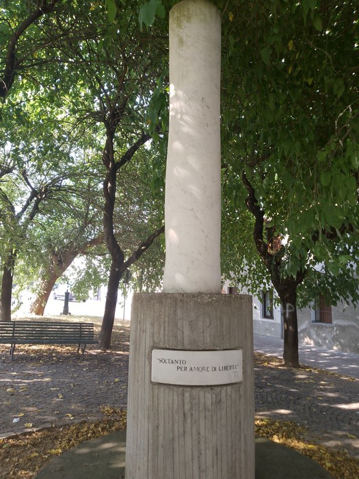 Monumento a Brambilla, colonna bianca circondata da alberi in un verde parco pubblico.