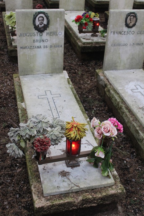 Tombe commemorative con fiori e candele, dedicate ai caduti per la Libertà. Atmosfera di rispetto e memoria.