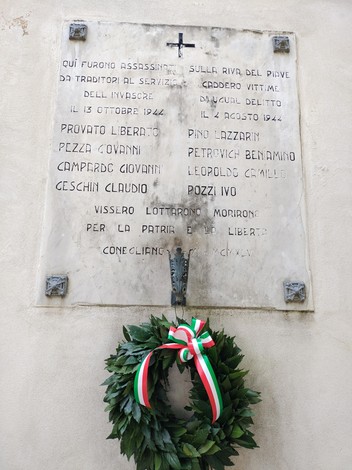 Lapide commemorativa dedicata ai partigiani fucilati, con corona di alloro e nastri tricolore.