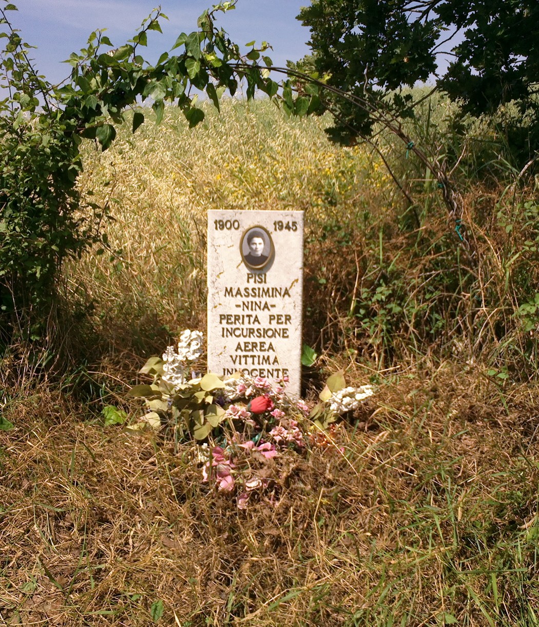 Cippo commemorativo dedicato a Massimina Pisi, vittima di un'incursione, 1900-1945, immerso nella natura.