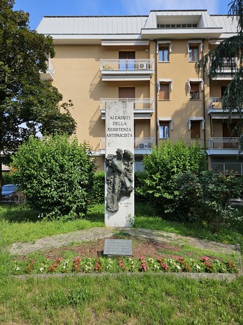 Monumento alla Resistenza, con scultura e iscrizione, circondato da un giardino e edifici residenziali.