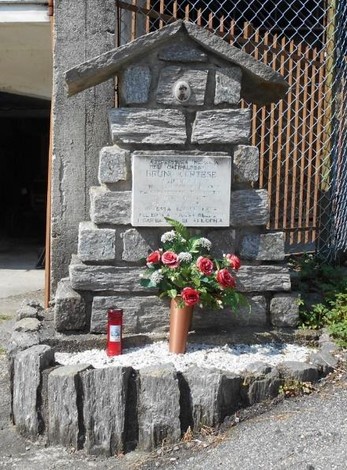Monumento a Cortese, dedicato alla memoria, con decorazioni floreali e candele in un contesto naturale.