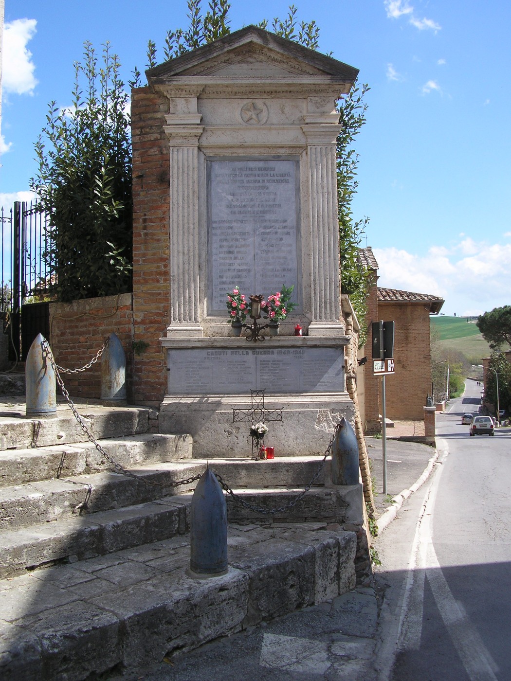 Tabernacolo ai caduti di Torrenieri, monumento commemorativo con decorazioni floreali e iscrizioni in un contesto rurale.