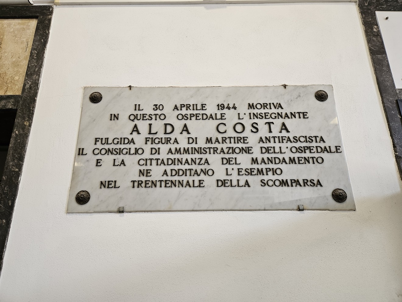 Lapide commemorativa in memoria di Alda Costa, insegnante e martire antifascista, situata in un ospedale.