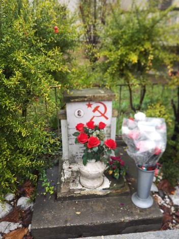 Monumento a Capucci: cippo commemorativo con fiori, simboli e decorazioni in un giardino curato.