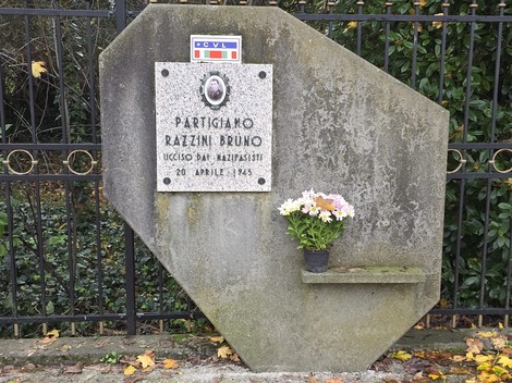 Monumento commemorativo a Razzini Bruno, con dedica e decorazione floreale, situato in un'area verde.