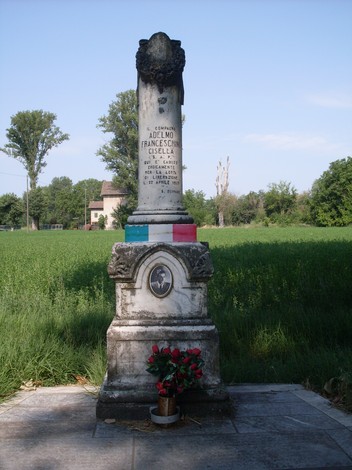 Cippo commemorativo dedicato a Adalmo Franceschini in un contesto verde e tranquillo.