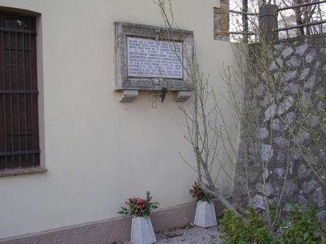 Lapide commemorativa di Niccioleta, situata su un muro con fiori ai piedi, in un contesto tranquillo.