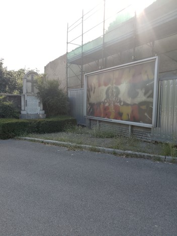 Monumento ai Martiri di Pessano con Bornago, circondato da vegetazione e recinzioni.