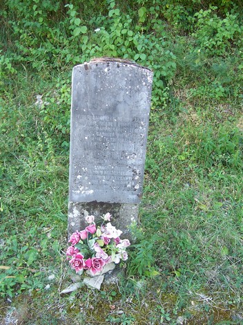 Cippo commemorativo in pietra, adornato con fiori freschi, immerso nel verde naturale circostante.