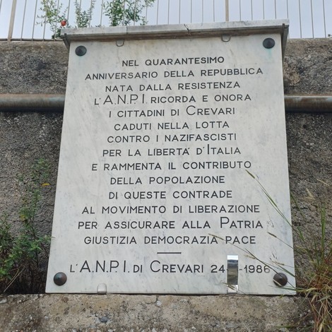 Lapide in marmo con iscrizione, fissata a una parete esterna in pietra.