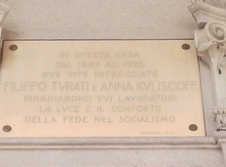 Targa in marmo con iscrizione, fissata con borchie alla facciata di un edificio.