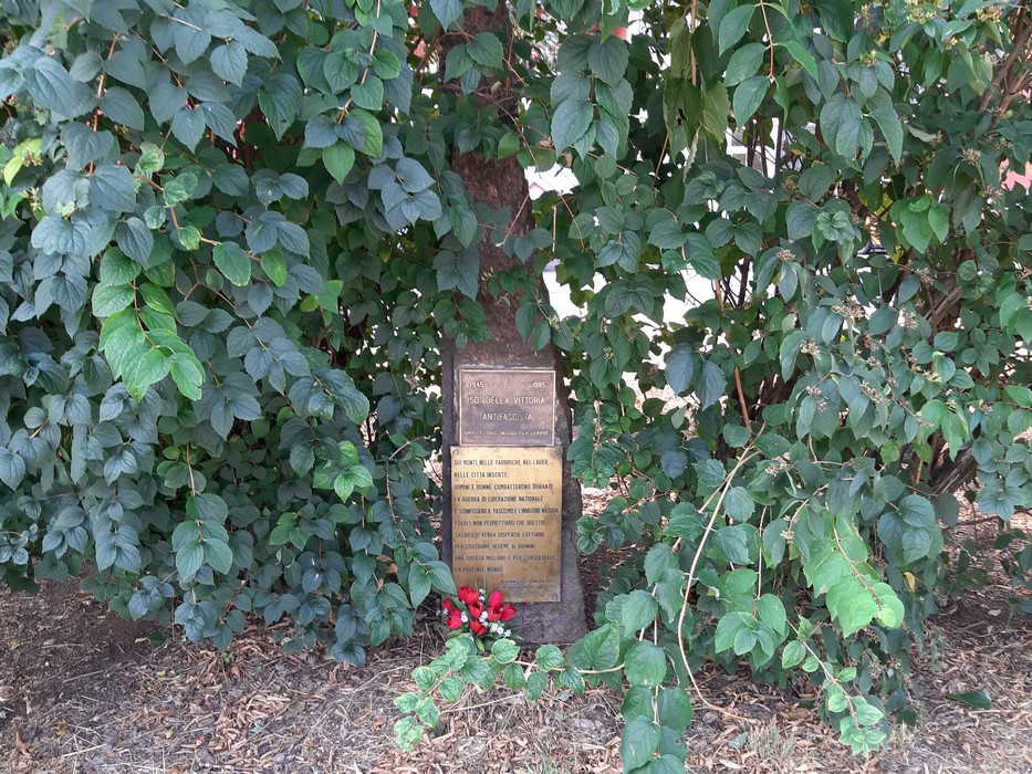 Cippo commemorativo circondato da vegetazione, dedicato al 40° e 50° anniversario della Resistenza.
