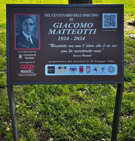 Targa commemorativa per Giacomo Matteotti, con un'immagine del politico e un QR code, posizionata in un'area verde.