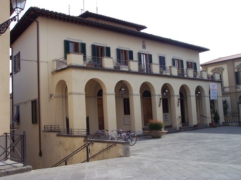 Immagine della facciata di un edificio storico con portico, biciclette parcheggiate e una piazza circostante.