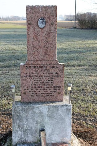 Cippo commemorativo di Mondadori, con iscrizioni e foto, situato in un ampio campo.