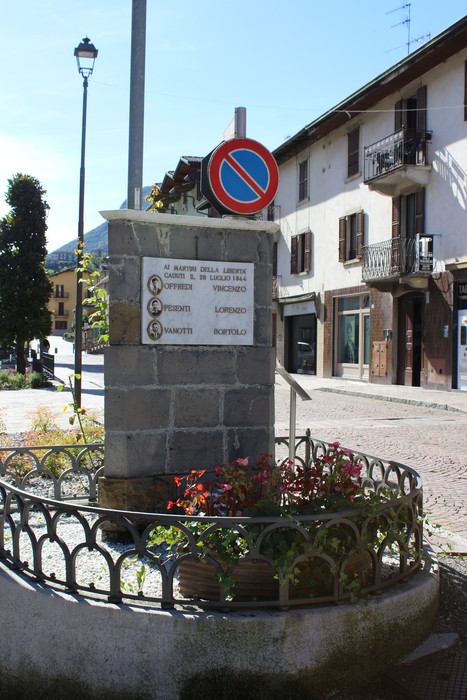 Cippo commemorativo a Offredi, dedicato a Pesenti e Vanotti, con decorazioni floreali e segnaletica stradale.