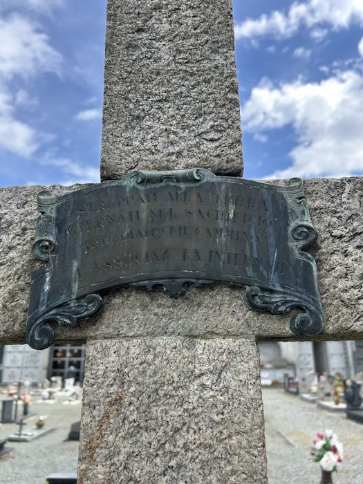 Croce dedicata agli internati militari, simbolo di memoria e riconoscenza. Cimitero con lapidi sullo sfondo.