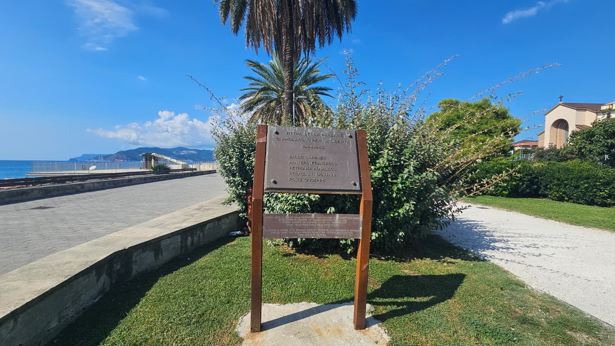Targa commemorativa dedicata ai caduti per la libertà, situata in un'area verde vicino al mare.