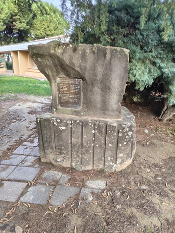 Monumento commemorativo dedicato ai deportati, situato in un'area verde con alberi e vegetazione.
