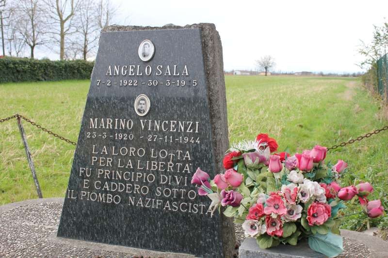 Cippo commemorativo dedicato ad Angelo Sala e Marino Vincenzi, con fiori sul monumento in un paesaggio aperto.