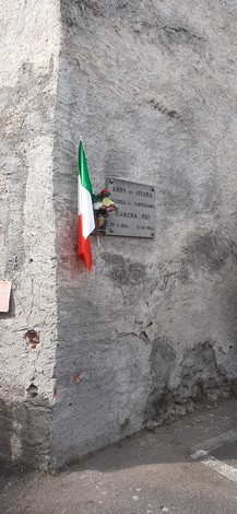 Lapide commemorativa con bandiera italiana, situata su un muro di pietra.