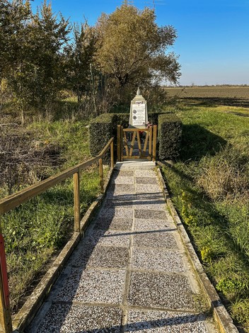 Sentiero panoramico che conduce al cippo commemorativo ai Fornasari, circondato da natura e campi aperti.