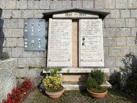 Monumento ai caduti di Castello Tesino, con iscrizioni commemorative su pietra e decorazioni floreali.