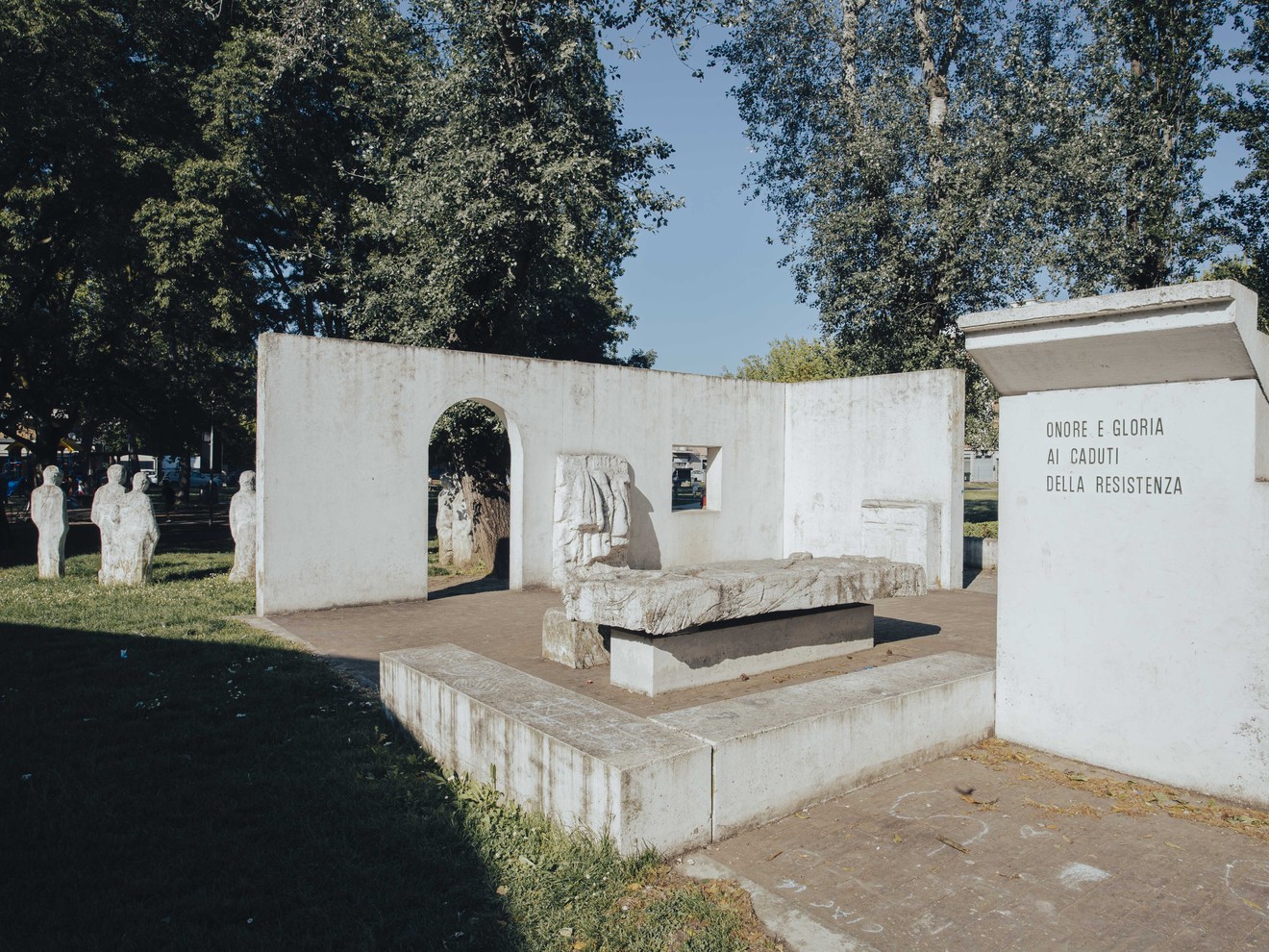 Monumento alla Resistenza con una struttura bianca e statue in un'area verde, simbolo di commemorazione.