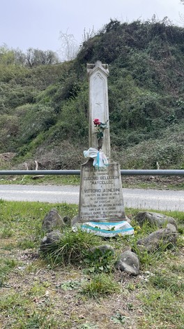 Cippo commemorativo dedicato a Bellini e Agnesini, circondato da vegetazione e pietre.