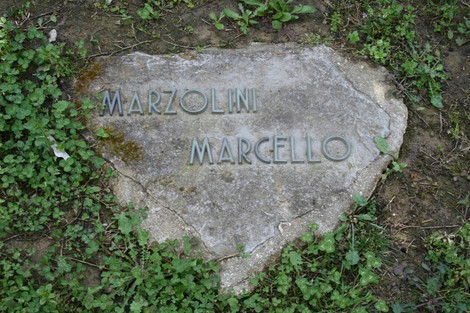 Monumento in pietra nel cimitero di Stia, dedicato a Marcello Marzolini, immerso nel verde.