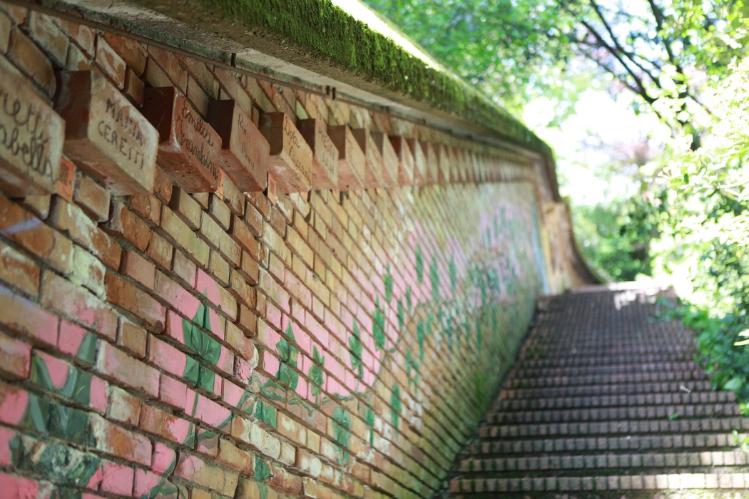 Fossato in mattoni con decorazioni artistiche, circondato da verde, che conduce al Monumento delle 128 partigiane.