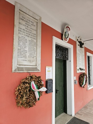 Lapide memoriale ai caduti della guerra 1940-45 con ghirlande di foglie secche e decorazioni tricolori.