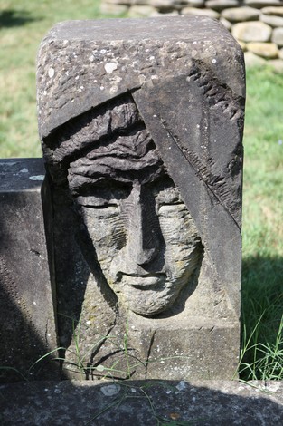 Monumento ai caduti della valle del Panaro, con un volto scolpito su una pietra in un contesto naturale.