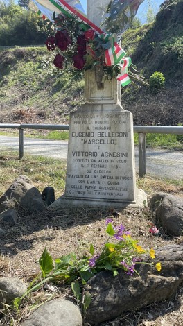 Cippo commemorativo dedicato a Eugenio Bellegoni e Vittorio Agnesini, con fiori e nastri tricolori.