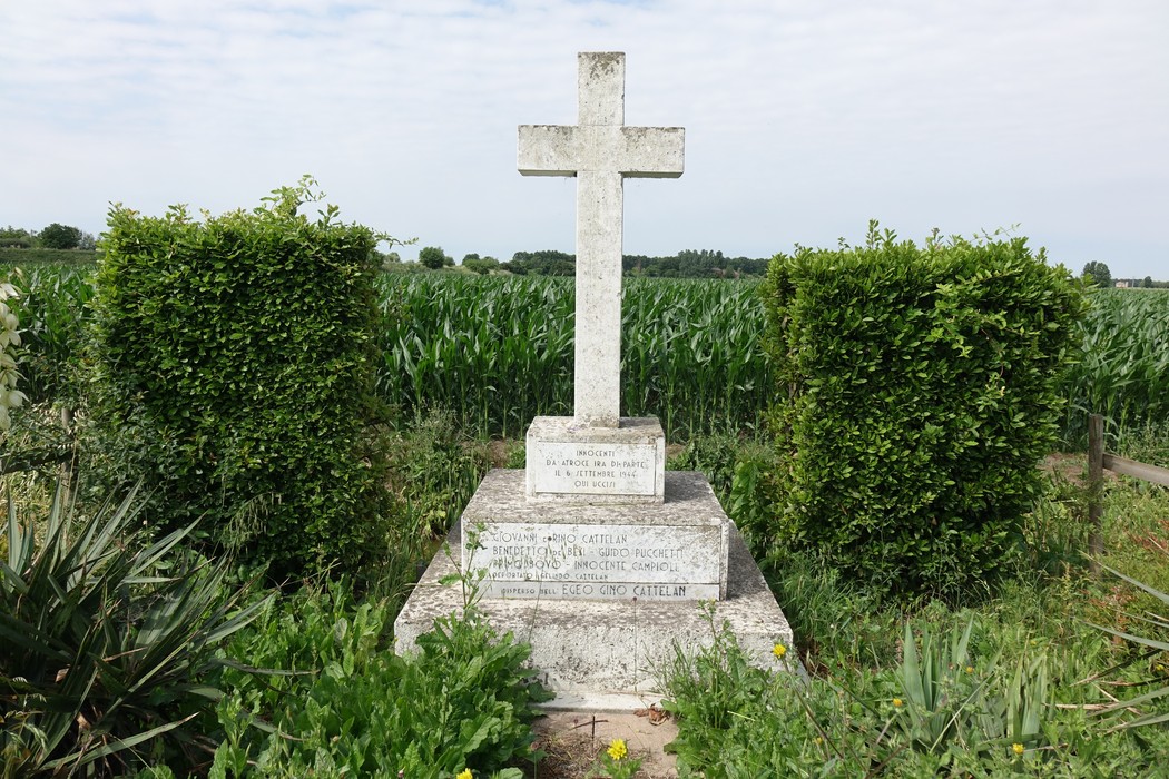 Croce commemorativa con siepi e verdeggianti campi sullo sfondo.