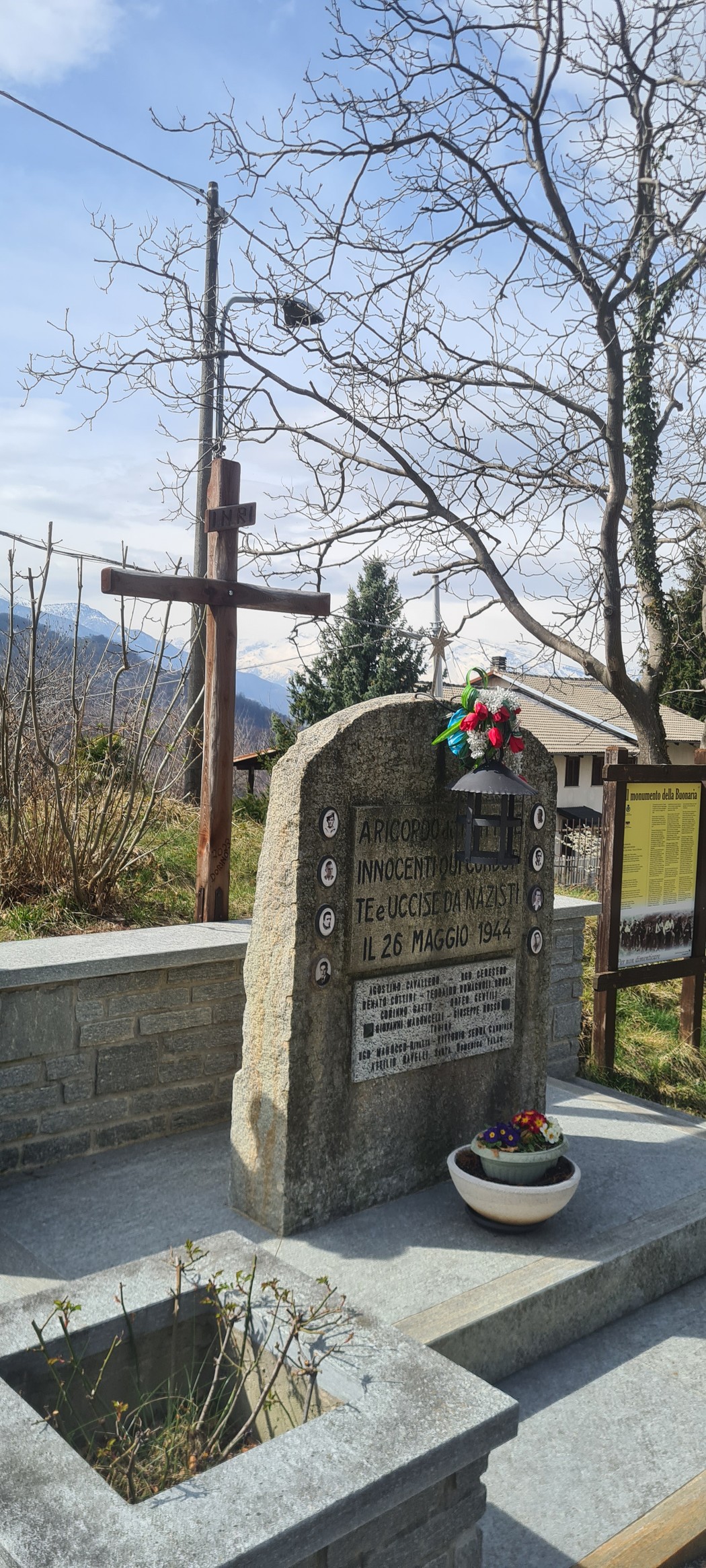 Monumento dedicato ai caduti della Buonaria, con una croce e decorazioni floreali in un paesaggio naturale.