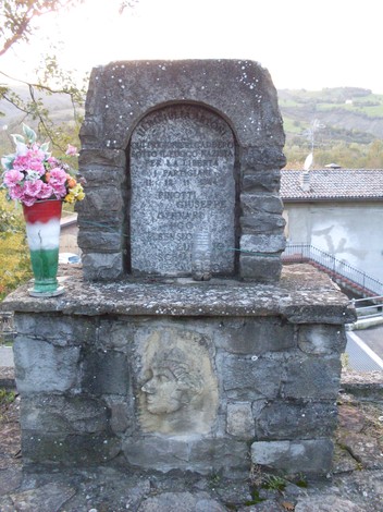 Monumento commemorativo dedicato a Pinotti, Gennari, Sensioni e Schianchi, con decorazioni floreali.
