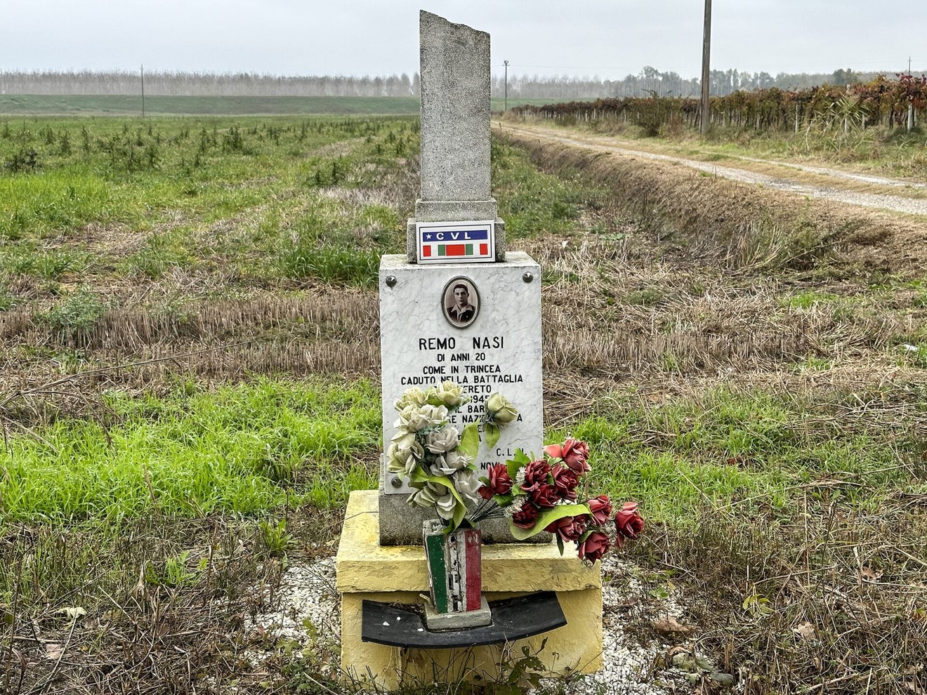 Cippo commemorativo dedicato a Remo Nasi, situato in una campagna tranquilla.