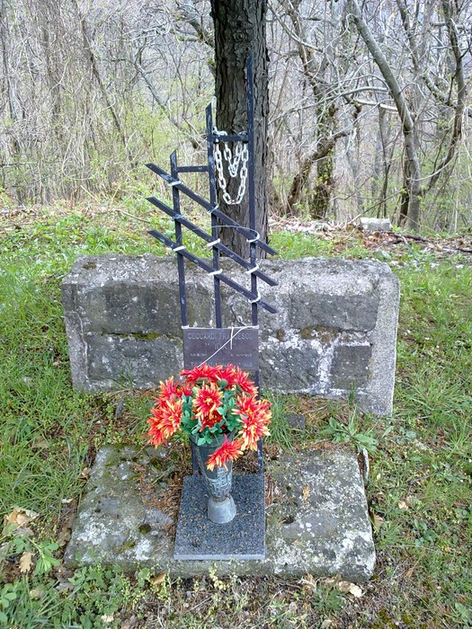 Cippo commemorativo a Ceccardi, decorato con fiori artificiali e situato in un'area naturale.