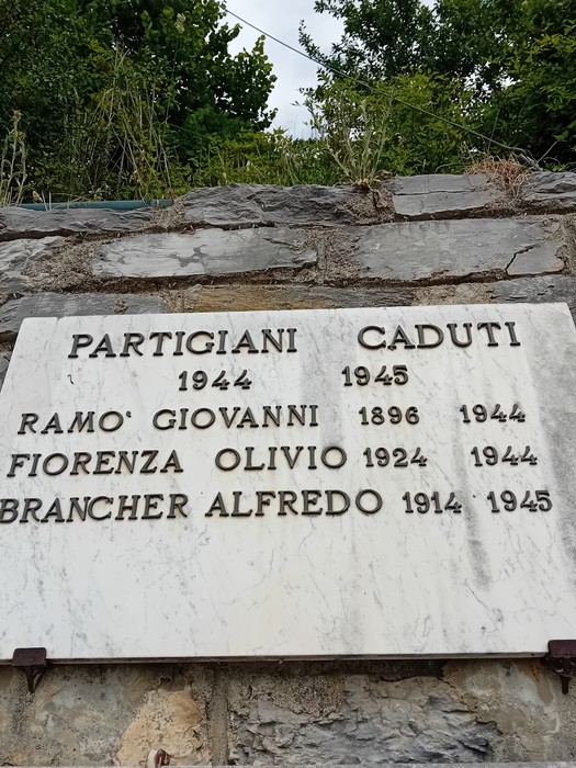 Monumento ai caduti, dedicato ai partigiani con i nomi incisi su una lastra di marmo, circondato da vegetazione.