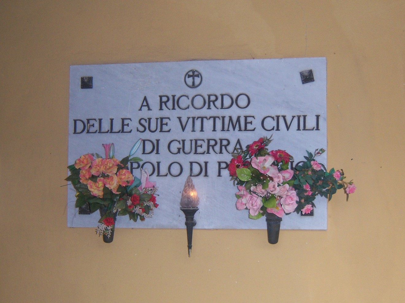 Lapide commemorativa per le vittime civili di Piteccio, adornata con fiori e una fiaccola.