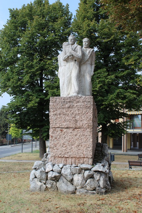 Monumento alla Resistenza con tre figure scolpite su una base in pietra, circondato da alberi e un'area verde.