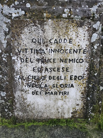 Cippo a Benaglia con iscrizione commemorativa su sfondo roccioso e muschioso, simbolo di memoria storica.