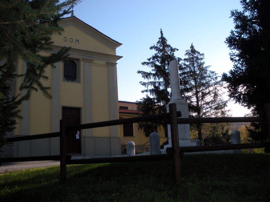 Cippo commemorativo dedicato ai caduti, con alle spalle un edificio e alberi in un contesto naturale.