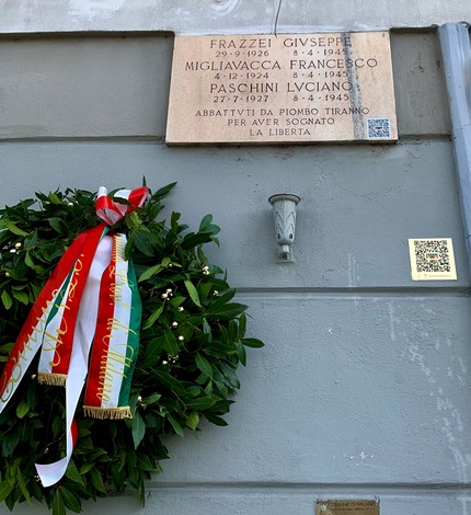 Lapide commemorativa dedicata a Paschini, Frazzei e Migliavacca, con corona di alloro e nastro tricolore.