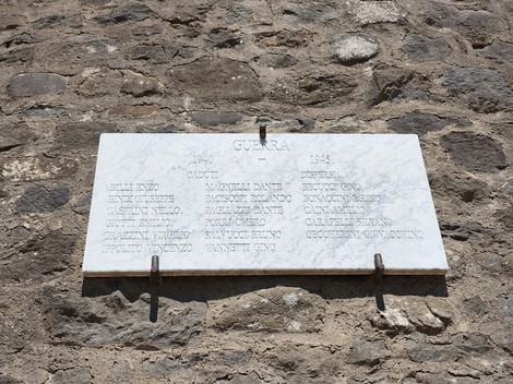 Lapide in marmo con iscrizione ai caduti di guerra, fissata su parete in pietra a vista.